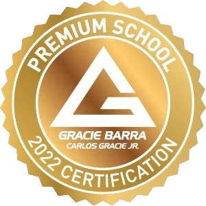 Gold badge with text: "Premium School, Gracie Barra Naperville, Carlos Gracie Jr., 2022 Certification," and a stylized "G" logo in the center, celebrating excellence in BJJ training.